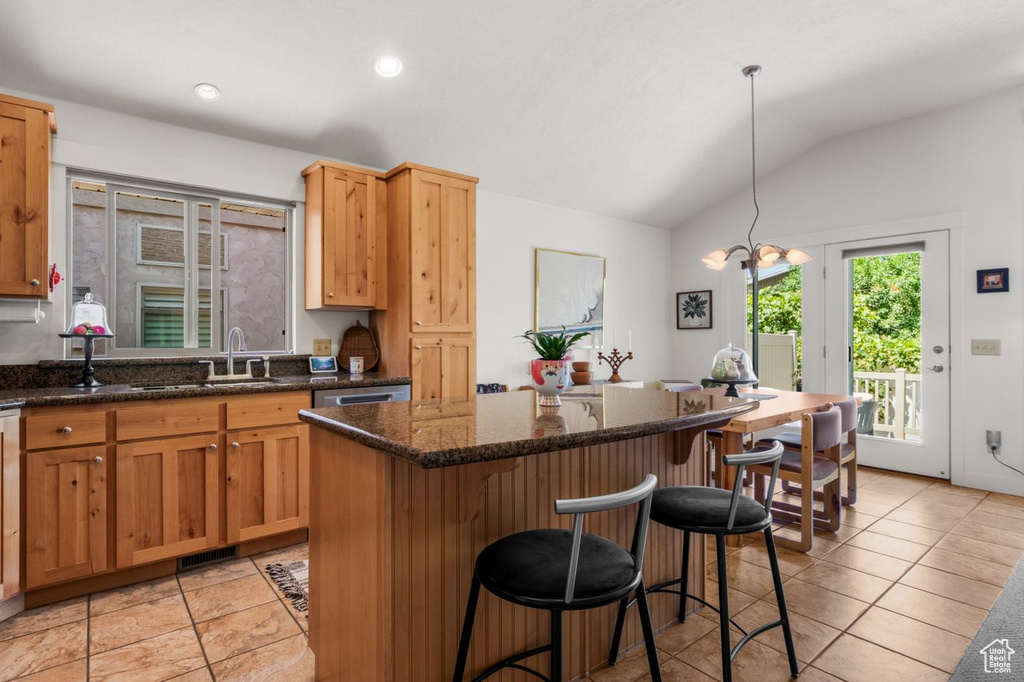 Kitchen featuring vaulted ceiling, a center island, a breakfast bar area, light tile patterned floors, and a sink