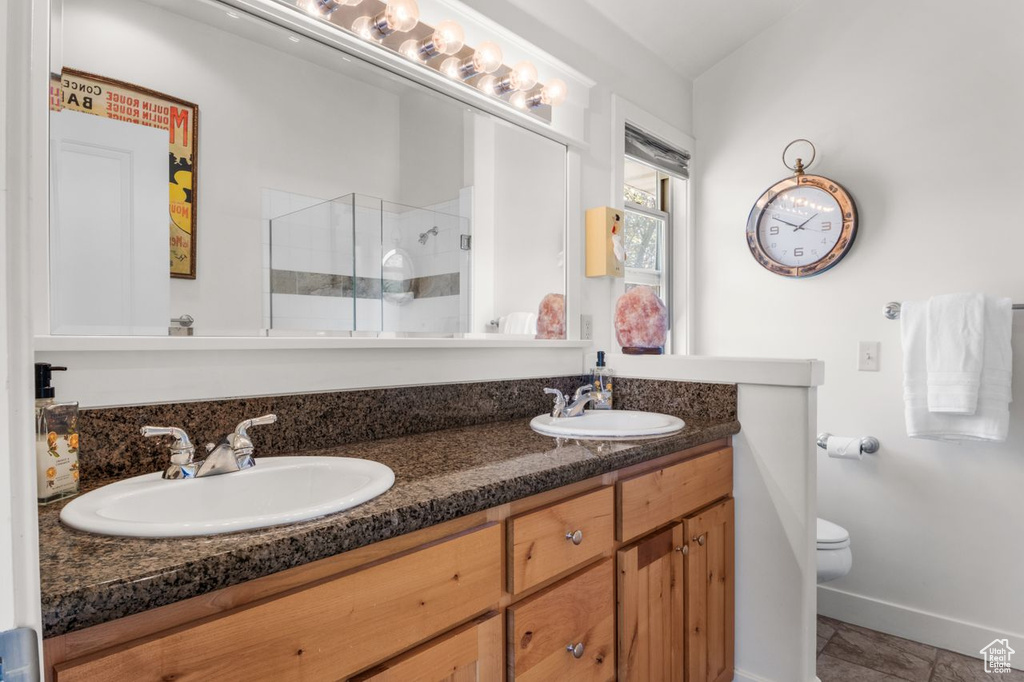 Full bathroom featuring toilet, a shower stall, double vanity, and baseboards