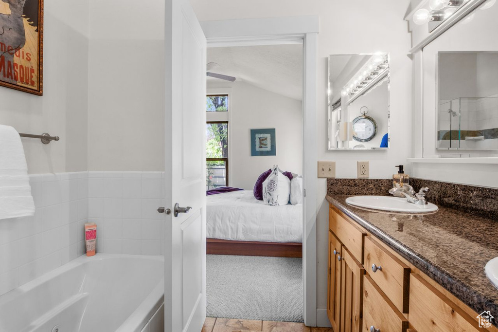 Full bath featuring double vanity, vaulted ceiling, connected bathroom, a bath, and tile patterned floors