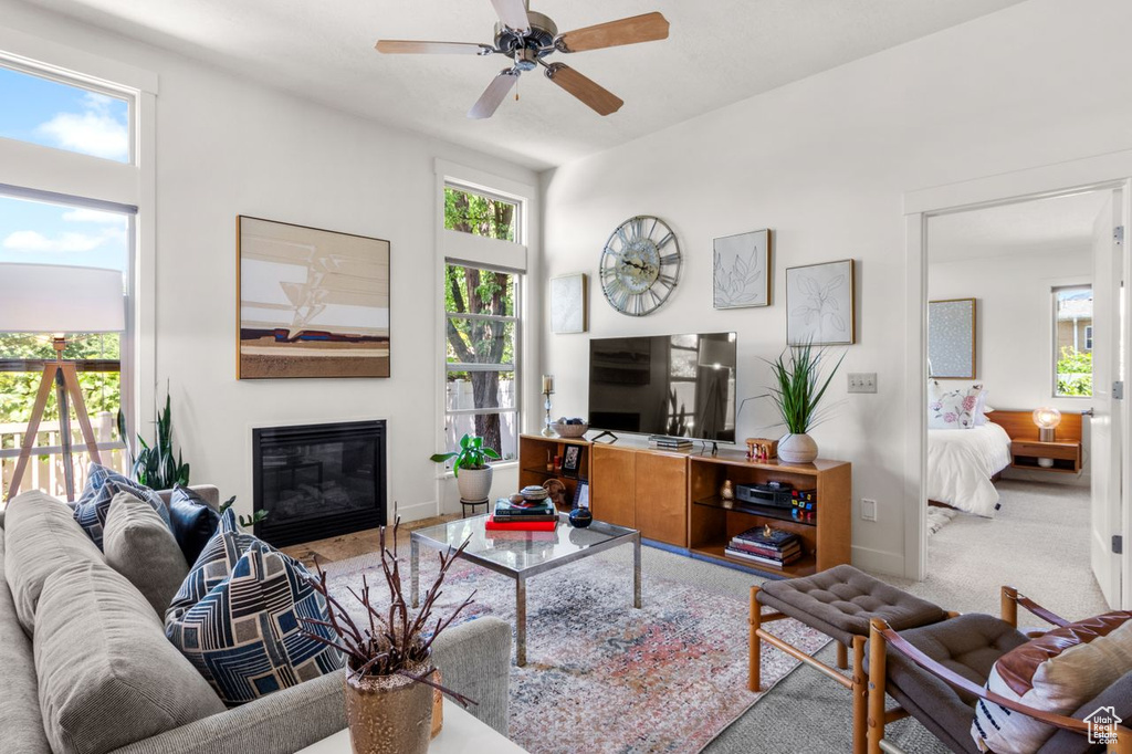 Living room featuring carpet flooring, ceiling fan, a glass covered fireplace, and baseboards