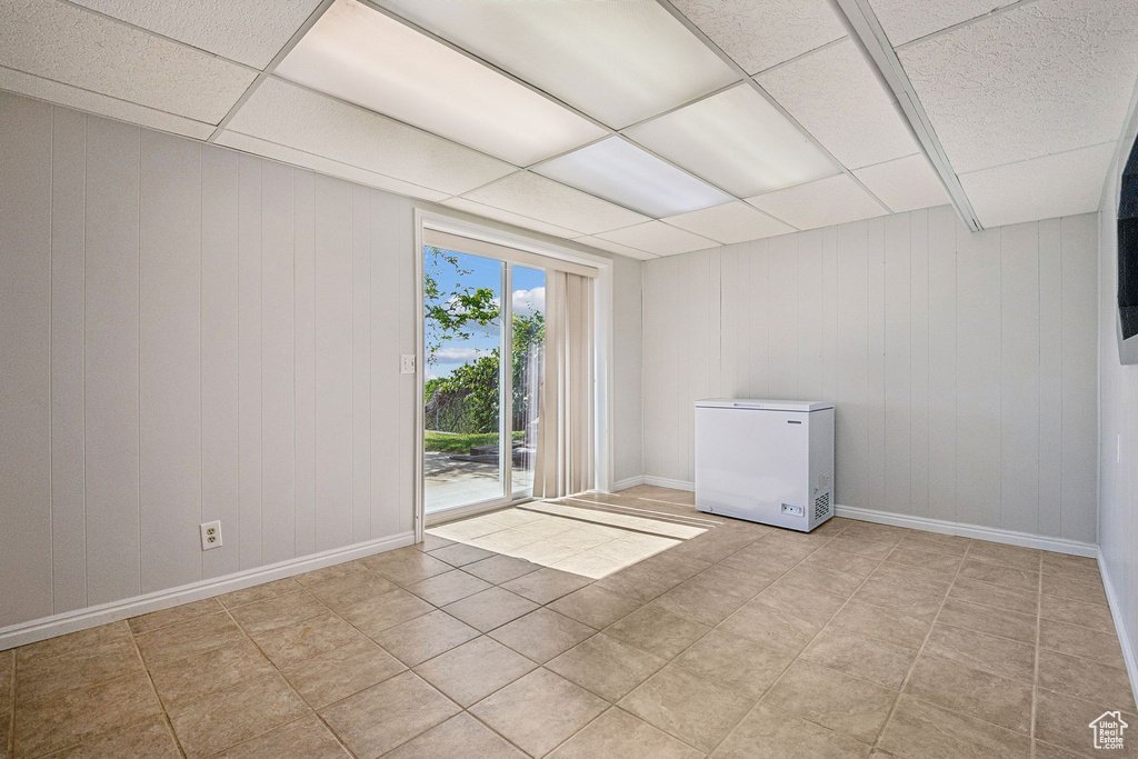 Unfurnished room with a paneled ceiling, baseboards, wood walls, and light tile patterned floors