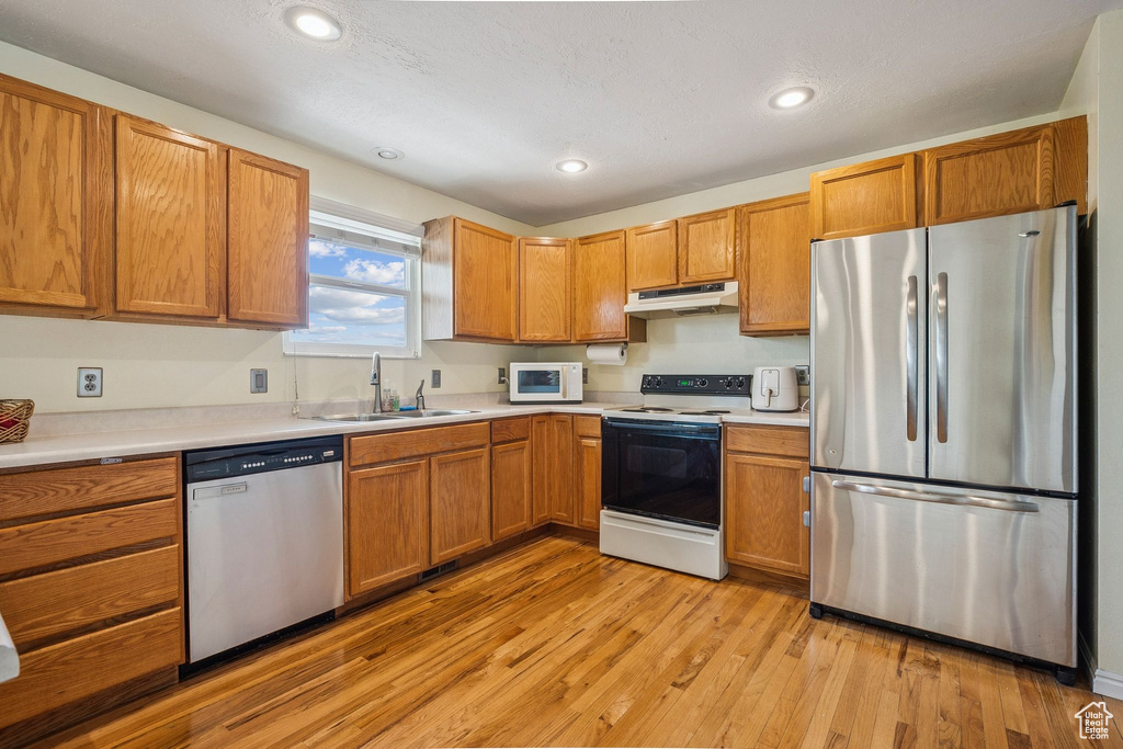 Kitchen featuring appliances with stainless steel finishes, a sink, under cabinet range hood, light countertops, and recessed lighting