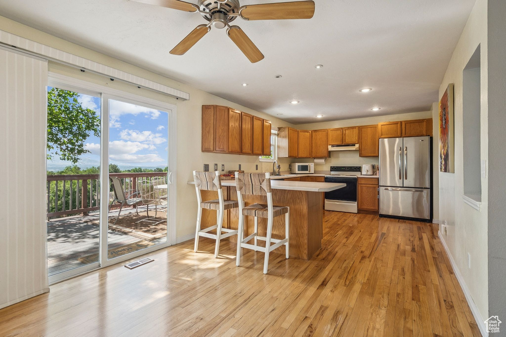 Kitchen featuring white appliances, light countertops, light wood-style floors, brown cabinetry, and recessed lighting