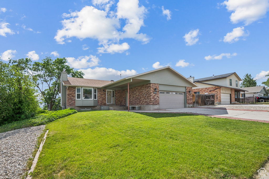 View of front facade featuring an attached garage, driveway, a front lawn, a chimney, and brick siding