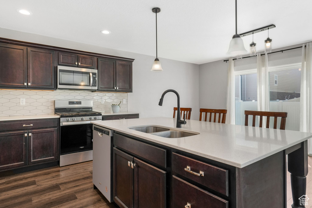Kitchen featuring stainless steel appliances, a sink, tasteful backsplash, dark wood finished floors, and hanging light fixtures