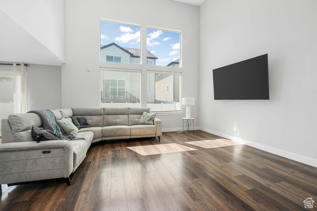 Living room featuring dark wood-style flooring, a high ceiling, and baseboards