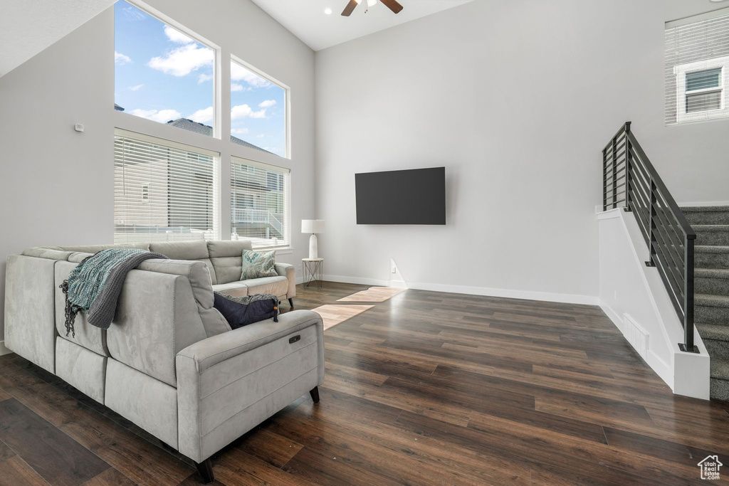 Living area featuring stairs, a ceiling fan, a high ceiling, dark wood-type flooring, and baseboards