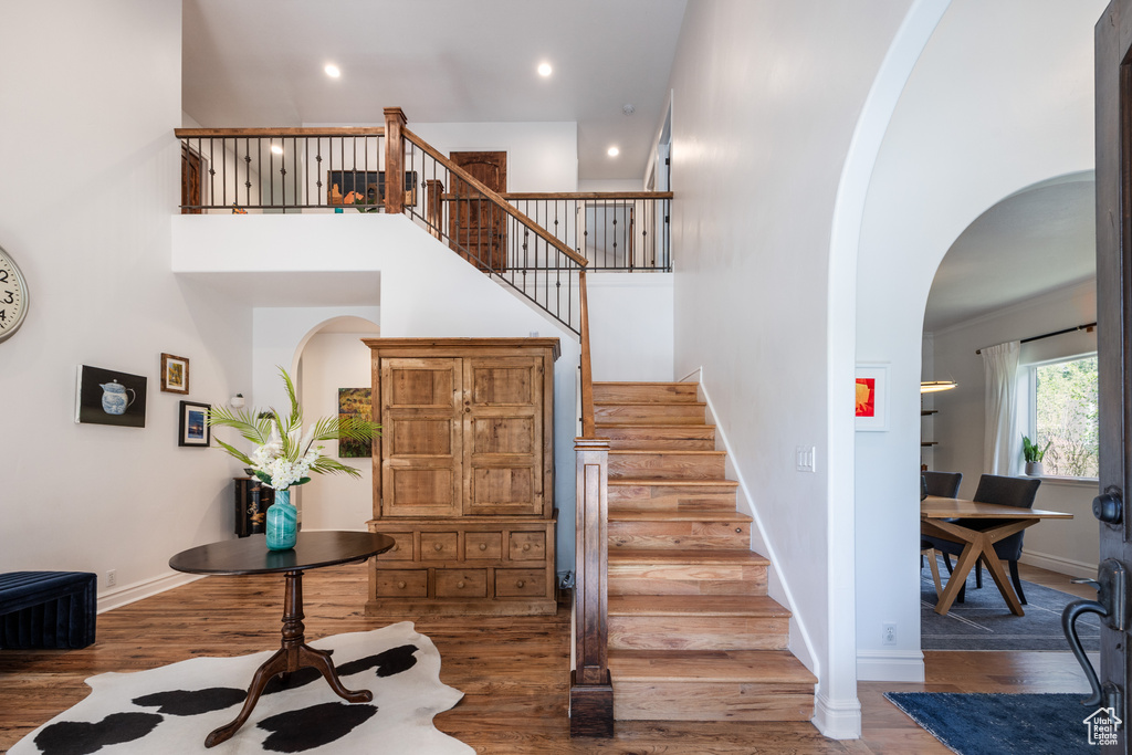 Staircase featuring arched walkways, wood finished floors, baseboards, a high ceiling, and recessed lighting