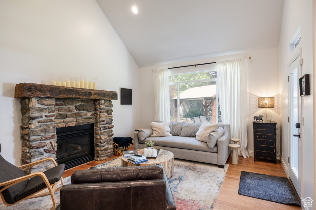 Living room with wood finished floors, high vaulted ceiling, and a stone fireplace