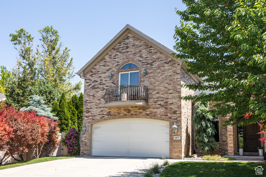 View of front of property with a balcony, brick siding, concrete driveway, and a garage
