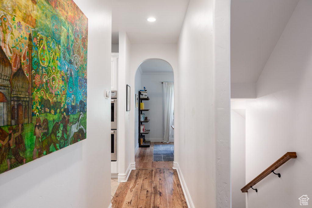 Hallway featuring arched walkways, light wood-type flooring, recessed lighting, and baseboards