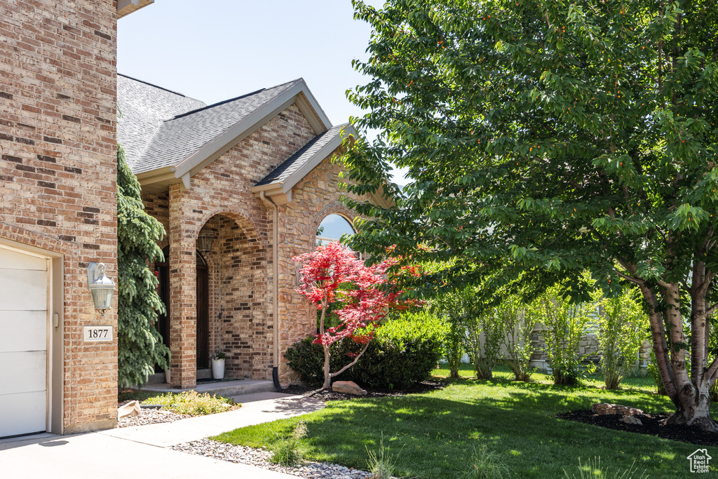 Property entrance with a yard, roof with shingles, and brick siding