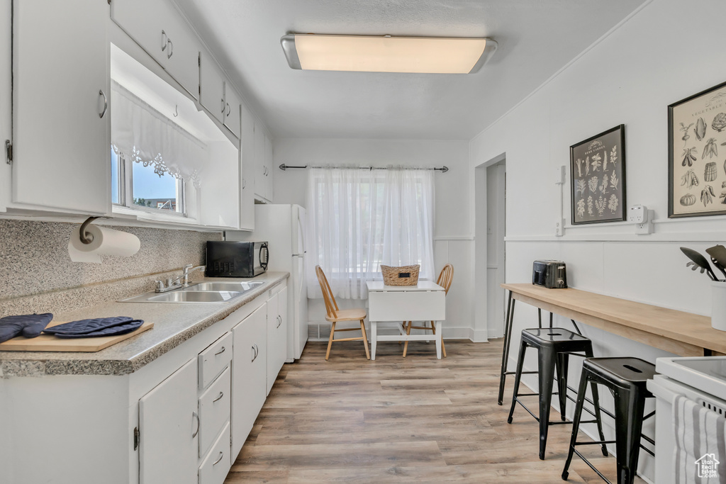 Kitchen with white appliances, a sink, white cabinetry, light countertops, and tasteful backsplash
