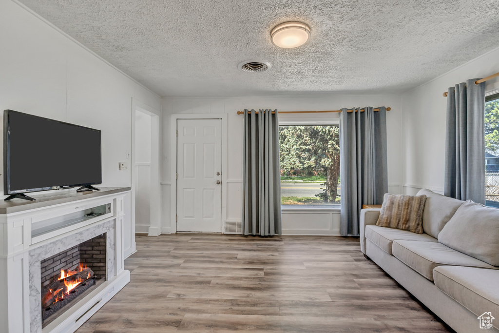 Living room with a textured ceiling, light wood-style floors, and a premium fireplace