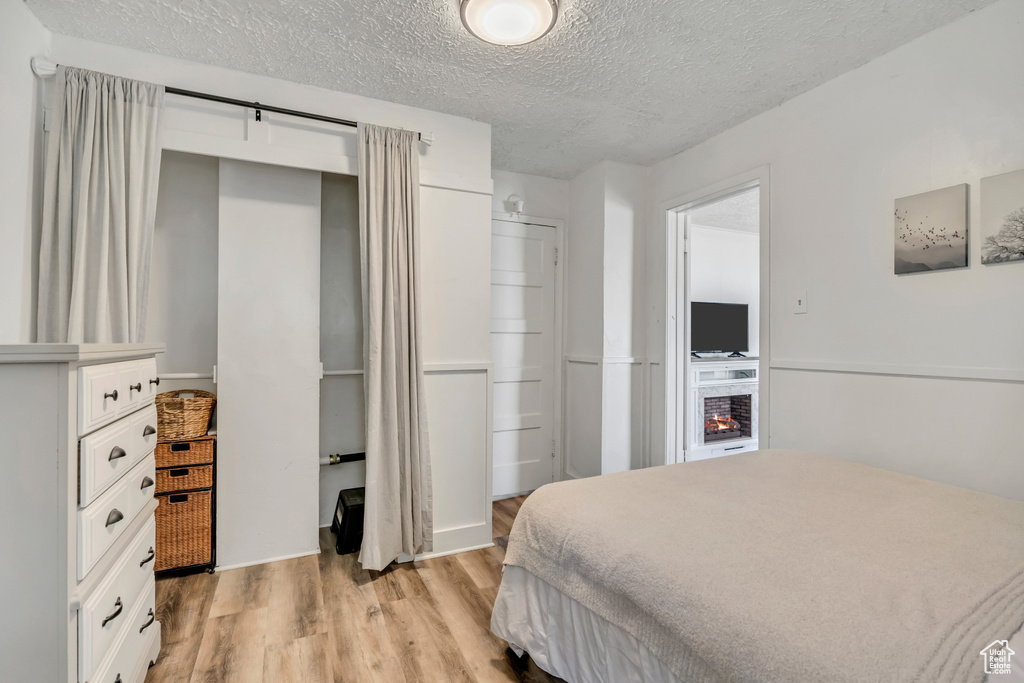 Bedroom featuring light wood-style floors, a textured ceiling, a closet, and a lit fireplace