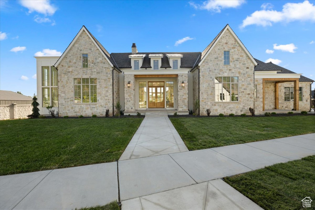 French country home with a chimney, a front lawn, stone siding, and french doors