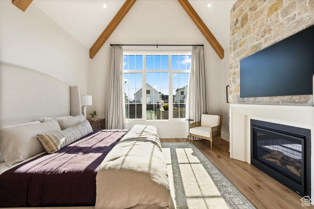 Bedroom featuring a glass covered fireplace, wood finished floors, beamed ceiling, and high vaulted ceiling