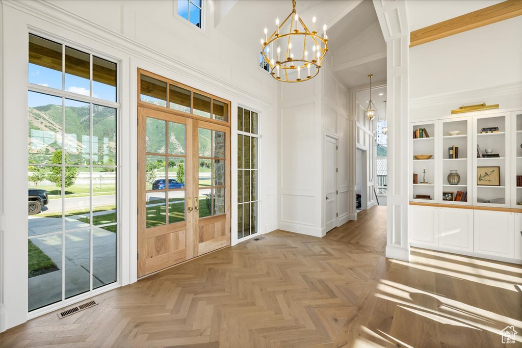 Entrance foyer featuring french doors, a decorative wall, a high ceiling, and a chandelier