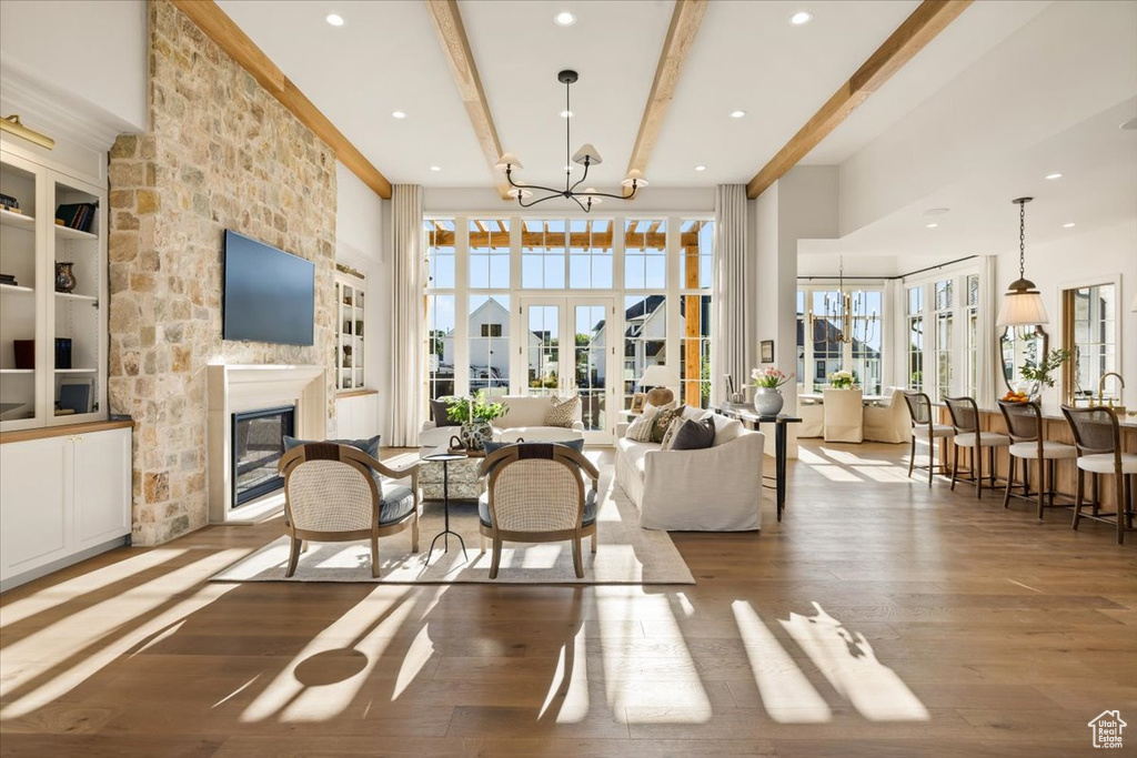 Living area with beam ceiling, wood finished floors, a chandelier, a fireplace, and a high ceiling