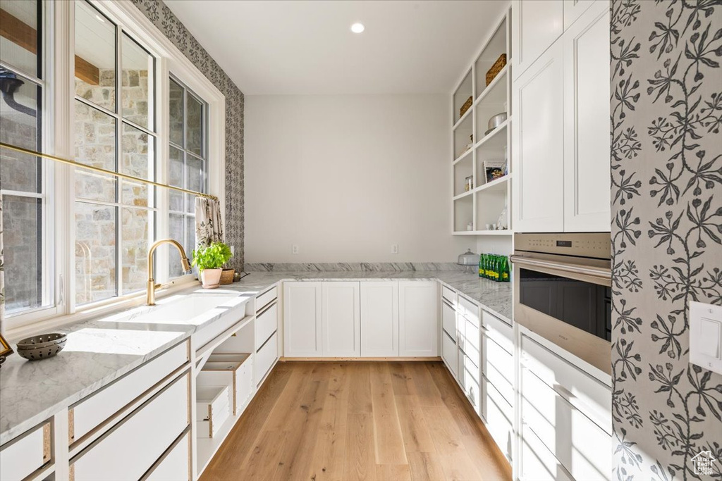Kitchen with light wood-style flooring, open shelves, stainless steel oven, light stone counters, and recessed lighting