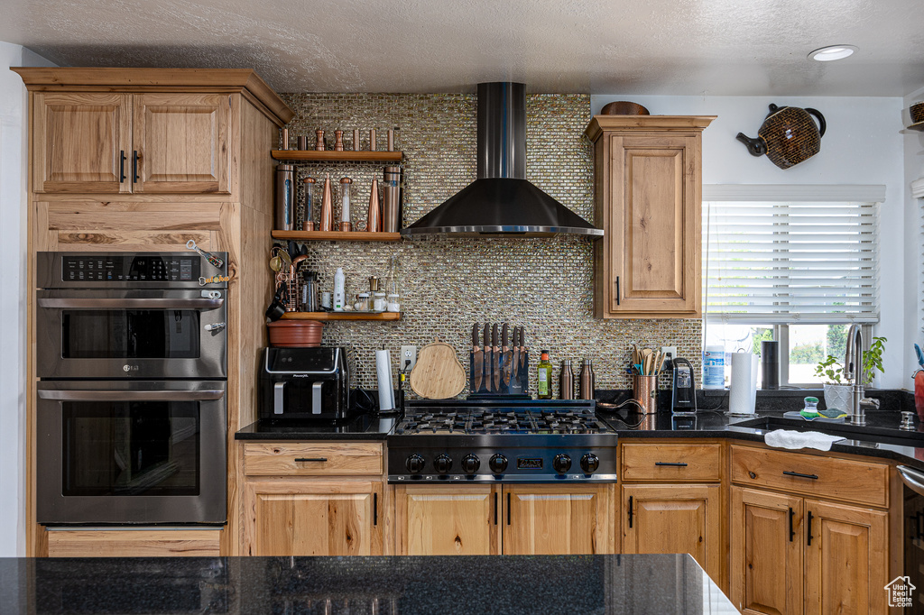 Kitchen with wall chimney range hood, double oven, gas cooktop, tasteful backsplash, and a textured ceiling