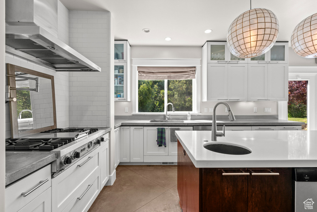 Kitchen featuring wall chimney range hood, a sink, tile patterned flooring, stainless steel gas stovetop, and decorative light fixtures