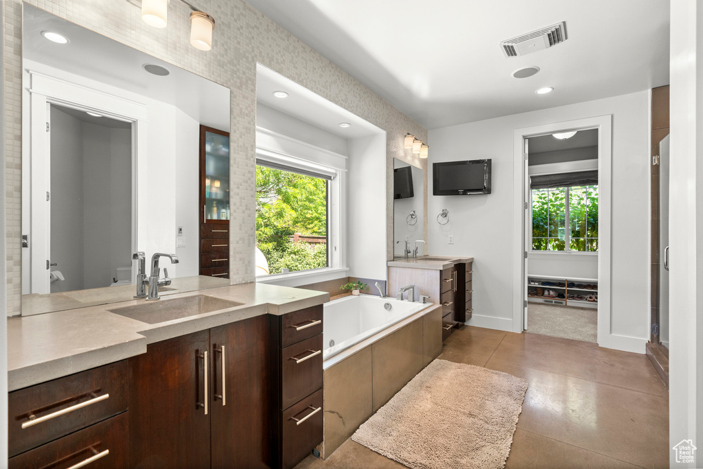 Bathroom with two vanities, a garden tub, baseboards, and recessed lighting