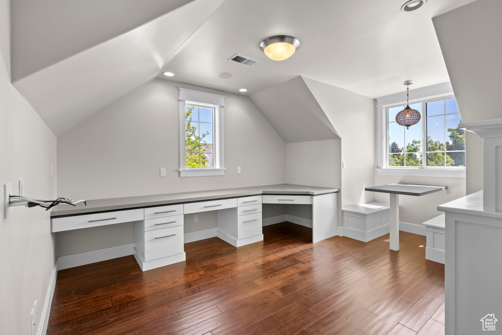 Unfurnished office featuring dark wood-style flooring, built in desk, vaulted ceiling, and baseboards