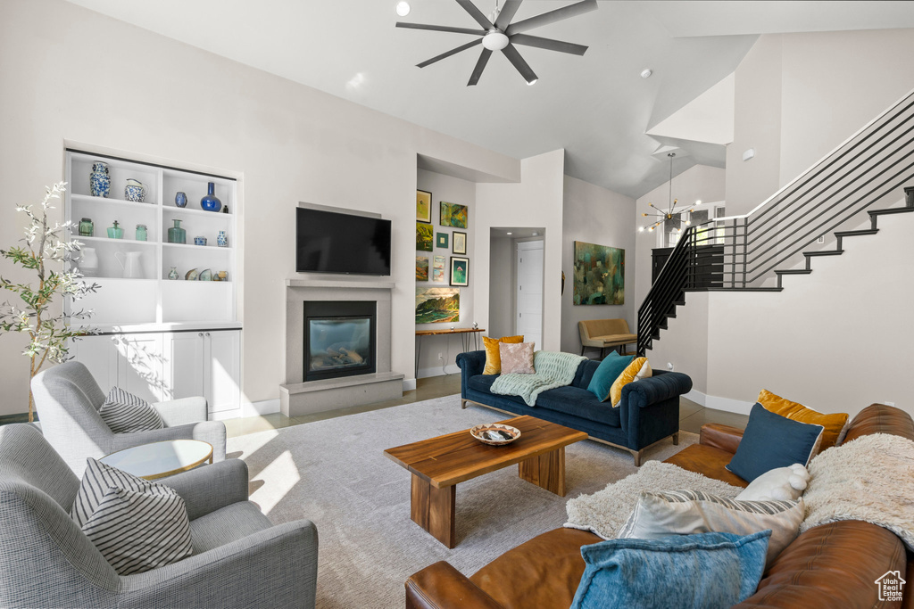 Living area featuring stairs, a ceiling fan, high vaulted ceiling, a glass covered fireplace, and a chandelier