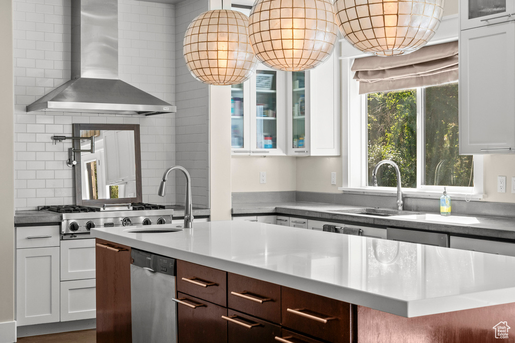 Kitchen with wall chimney exhaust hood, a sink, white cabinetry, and glass insert cabinets