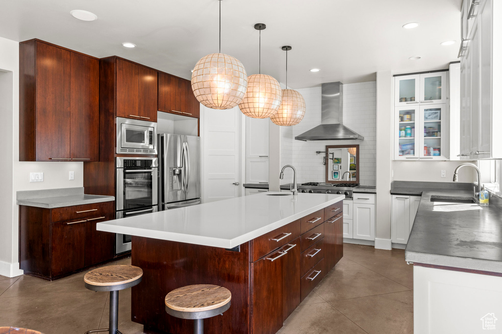 Kitchen featuring wall chimney exhaust hood, a sink, stainless steel appliances, a kitchen island with sink, and recessed lighting