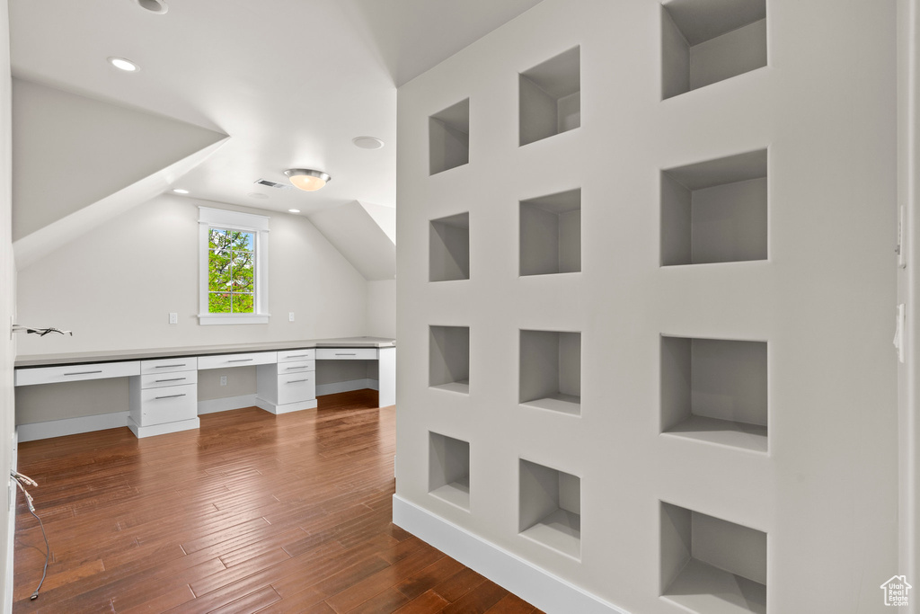 Unfurnished office with built in shelves, built in study area, dark wood-style floors, recessed lighting, and vaulted ceiling
