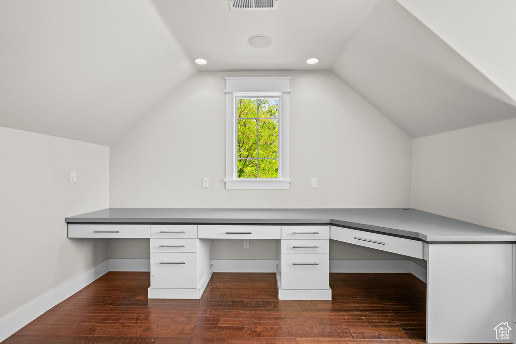 Unfurnished office featuring built in study area, dark wood-style floors, vaulted ceiling, and baseboards