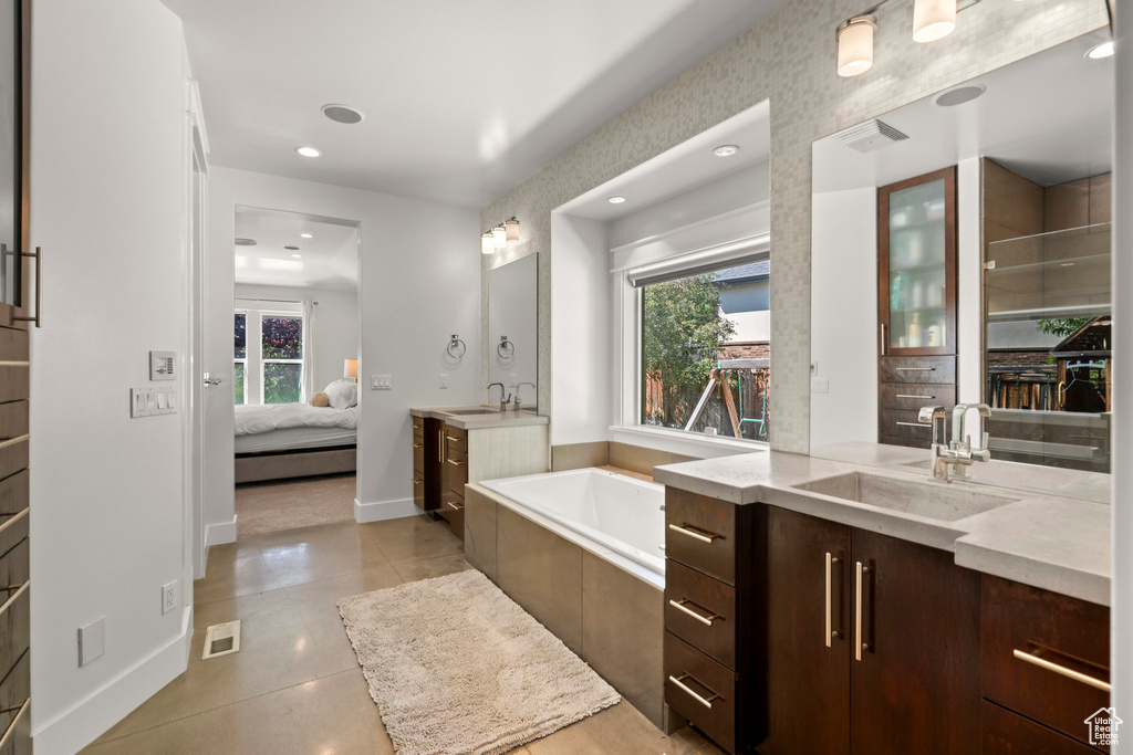 Ensuite bathroom featuring two vanities, plenty of natural light, a garden tub, baseboards, and recessed lighting