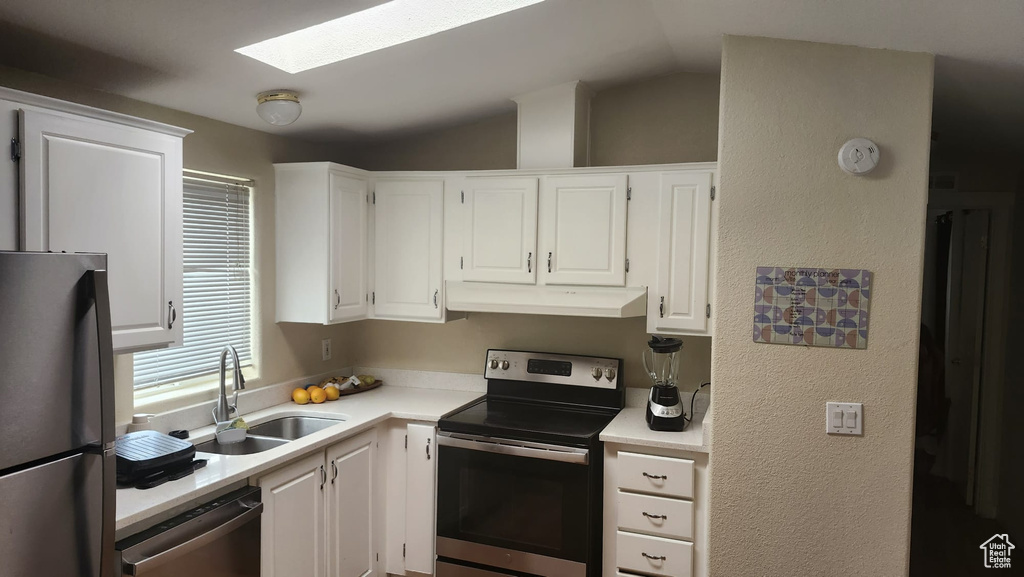 Kitchen with appliances with stainless steel finishes, under cabinet range hood, a sink, light countertops, and white cabinets