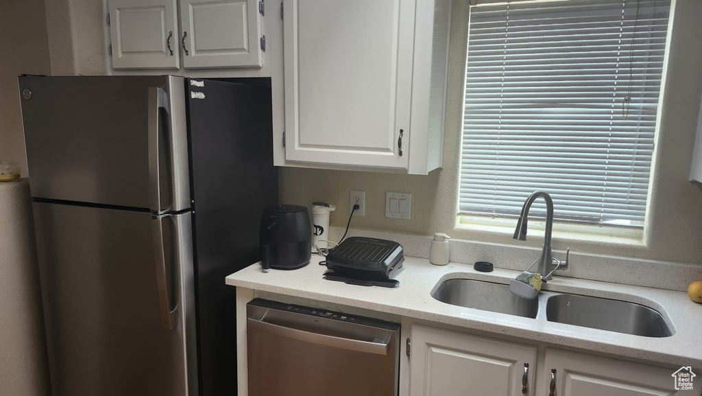 Kitchen featuring appliances with stainless steel finishes, a sink, white cabinetry, and light stone counters