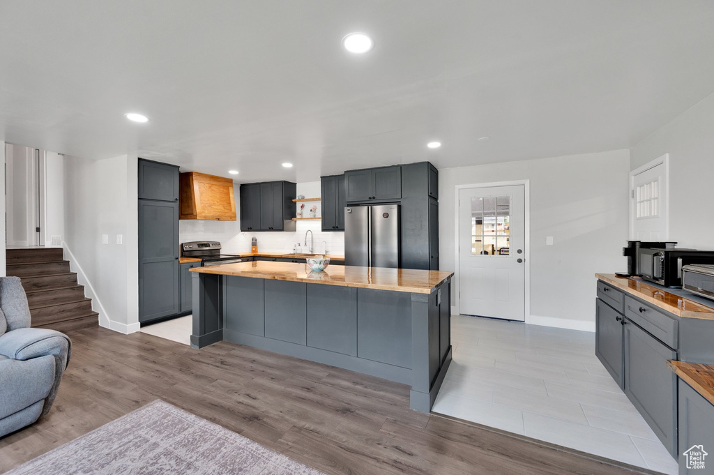 Kitchen featuring appliances with stainless steel finishes, a sink, baseboards, light wood finished floors, and a kitchen island