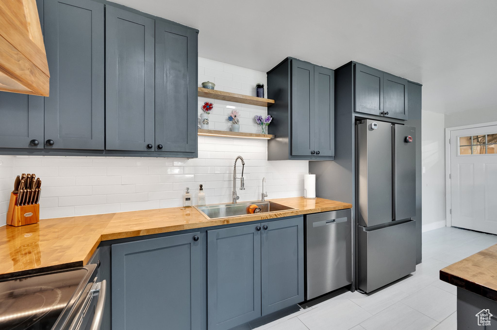 Kitchen featuring stainless steel appliances, butcher block countertops, a sink, tasteful backsplash, and open shelves