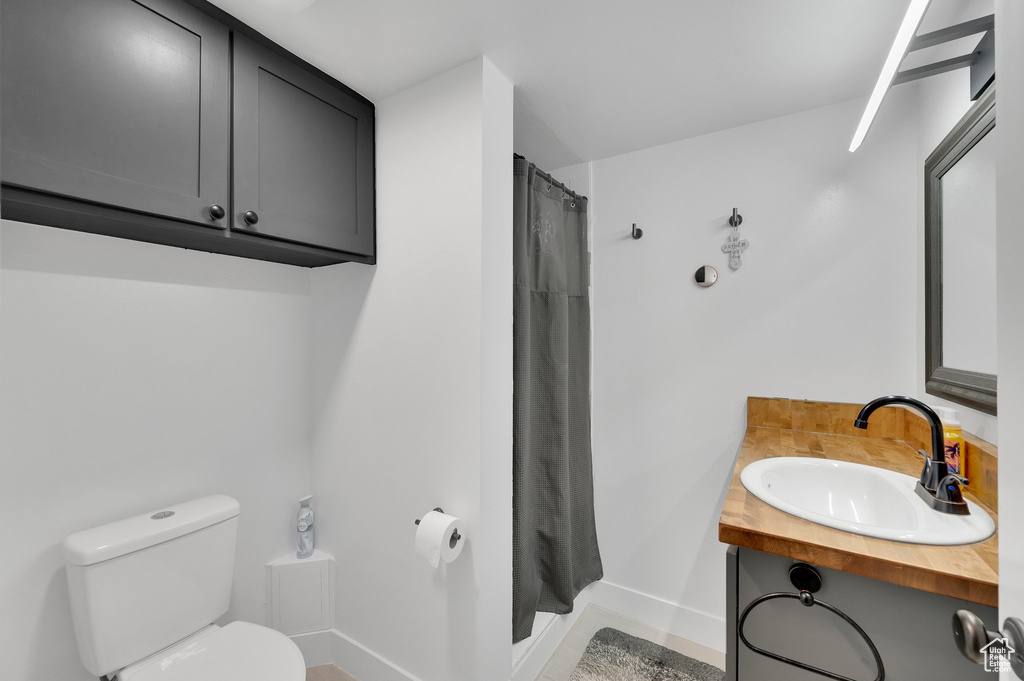 Full bath with toilet, vanity, curtained shower, and baseboards