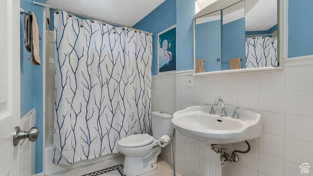 Bathroom with toilet, a sink, tile walls, tile patterned floors, and shower / bath combo
