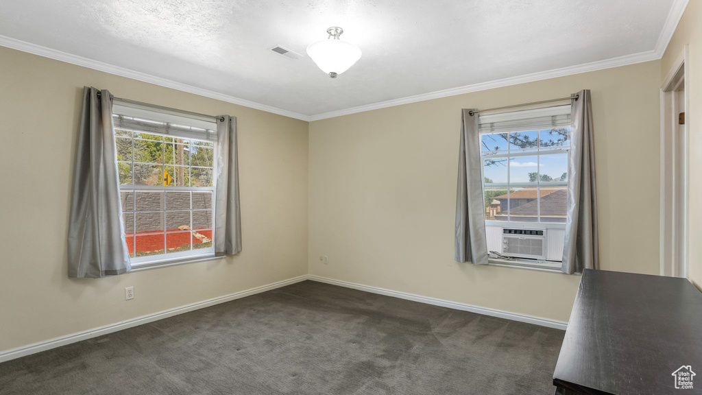 Spare room with healthy amount of natural light, ornamental molding, dark carpet, baseboards, and cooling unit