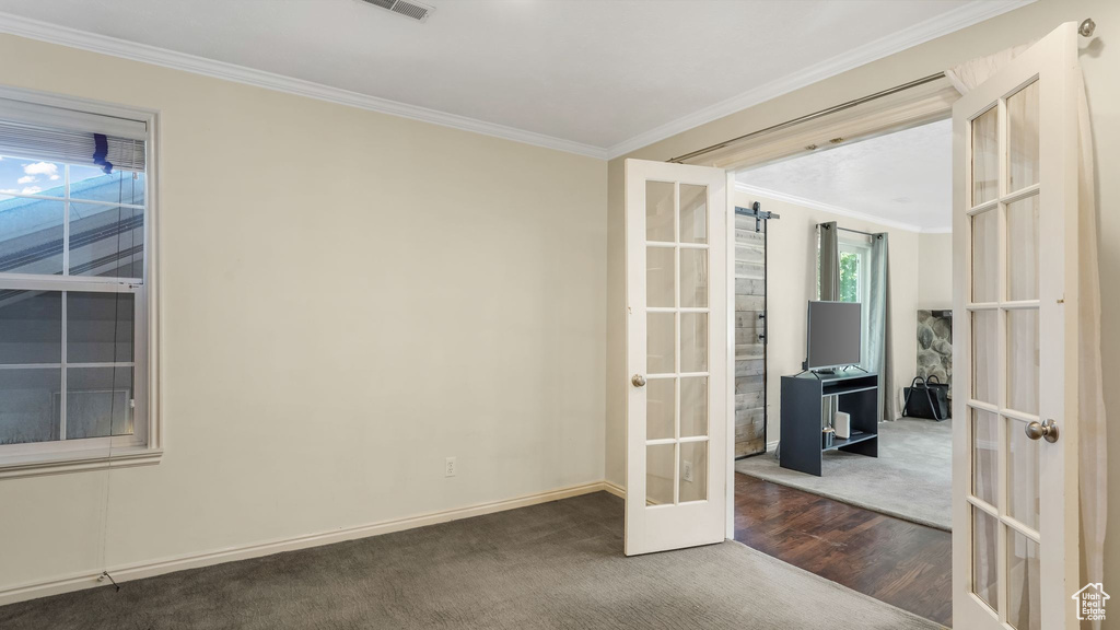 Empty room with french doors, carpet flooring, crown molding, baseboards, and wood finished floors
