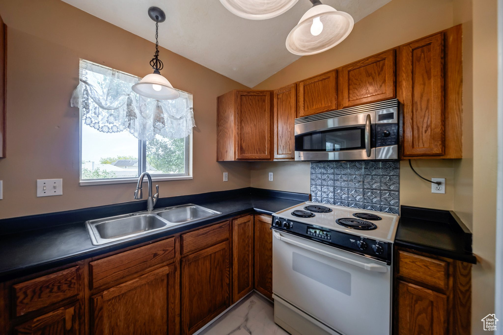 Kitchen featuring stainless steel microwave, white electric range, a sink, dark countertops, and brown cabinetry