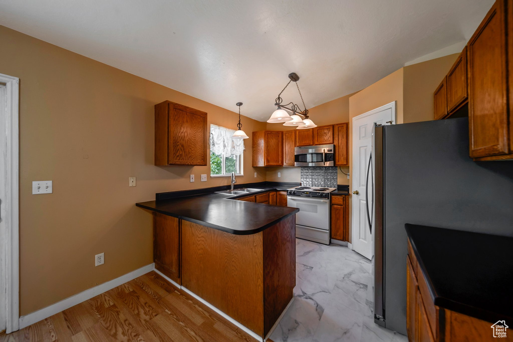 Kitchen featuring appliances with stainless steel finishes, a peninsula, a sink, dark countertops, and brown cabinets