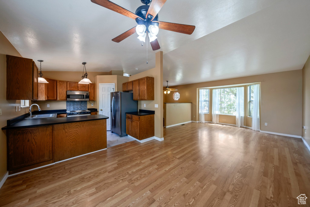 Kitchen with stainless steel appliances, open floor plan, vaulted ceiling, dark countertops, and a ceiling fan