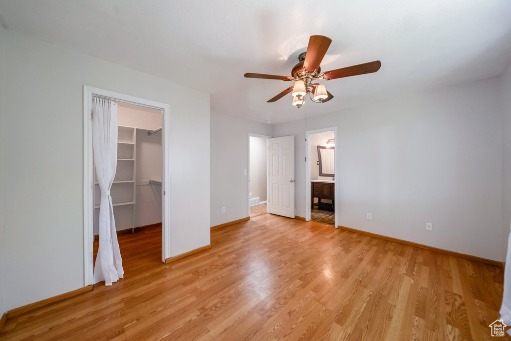 Unfurnished bedroom with a walk in closet, baseboards, light wood finished floors, a closet, and ceiling fan