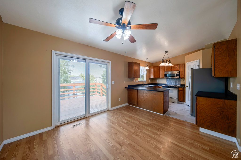 Kitchen featuring stainless steel microwave, a peninsula, brown cabinets, dark countertops, and light wood-style floors