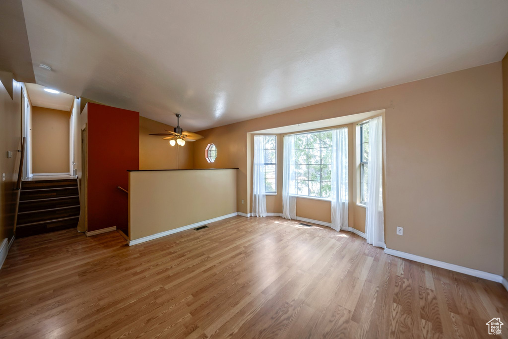 Unfurnished living room with wood finished floors, ceiling fan, baseboards, and stairway