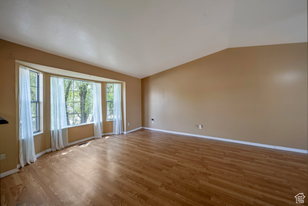 Empty room featuring vaulted ceiling, wood finished floors, and baseboards