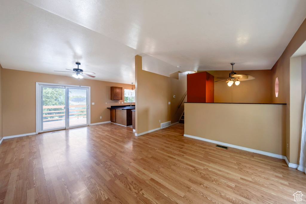 Unfurnished living room with a ceiling fan, light wood-style floors, baseboards, and stairs